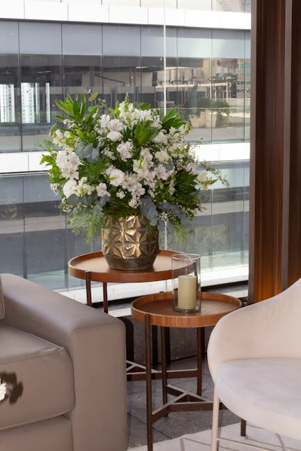 A floral arrangement featuring predominantly white flowers, including roses and lilies, with touches of greenery such as eucalyptus and ferns, arranged in a textured gold-toned ceramic vase. The bouqu
