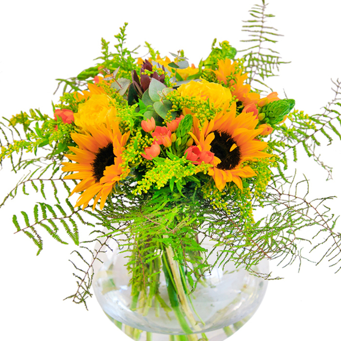 The first impression of this exquisite bouquet, arranged by a Hampstead Garden Suburb florist, is one of boundless sunshine and spirited joy. A dynamic display of radiant sunflowers anchors the design, their golden petals and chocolaty centers bringing to mind the sun-dappled meadows near Lyttelton Playing Fields. Enfolded within this warmth, plush garden roses in shades of buttery yellow unfurl in intricate spirals, offering a gentle contrast and an air of quiet luxury-much like the elegant residences tucked along Turner Close. Sprigs of ruby-red Hypericum berries glisten among the blooms, delivering striking bursts of colour that spark the eye and evoke communities gathering at local parks to celebrate the season. Cascading ferns and slender fillers in soft greens and yellows create a sense of dynamic motion, as though stirred by a Hampstead breeze wafting through the bouquet. Silvery eucalyptus leaves add a hint of coolness, both visual and aromatic, balancing the dominant gold tones with a touch of sophistication. All is contained within a transparent, fishbowl-style glass vase, which reveals the healthy tangle of stems in crystal-clear water, echoing the simplicity and style found in the gardens of Hampstead. This arrangement brims with freshness, warmth, and the distinctive touch of local craft-making it the perfect centrepiece for celebrations, tokens of friendship, or simply bringing the joyful spirit of Hampstead Garden Suburb into everyday life.